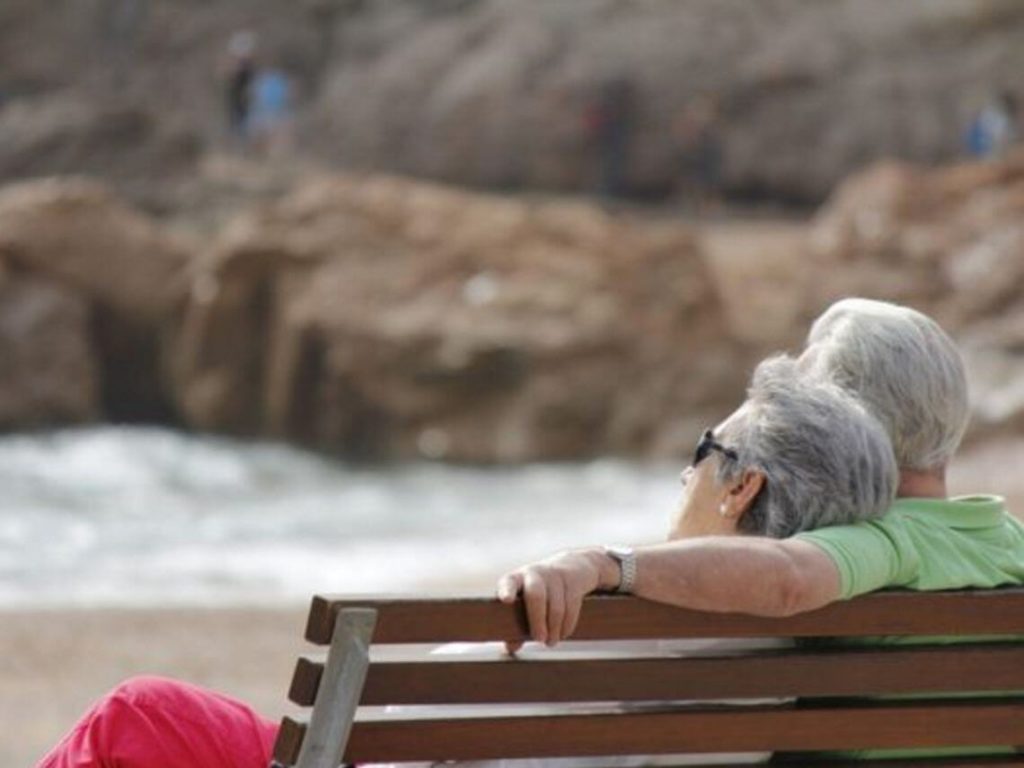 An elderly couple are looking out into the ocean on a bench