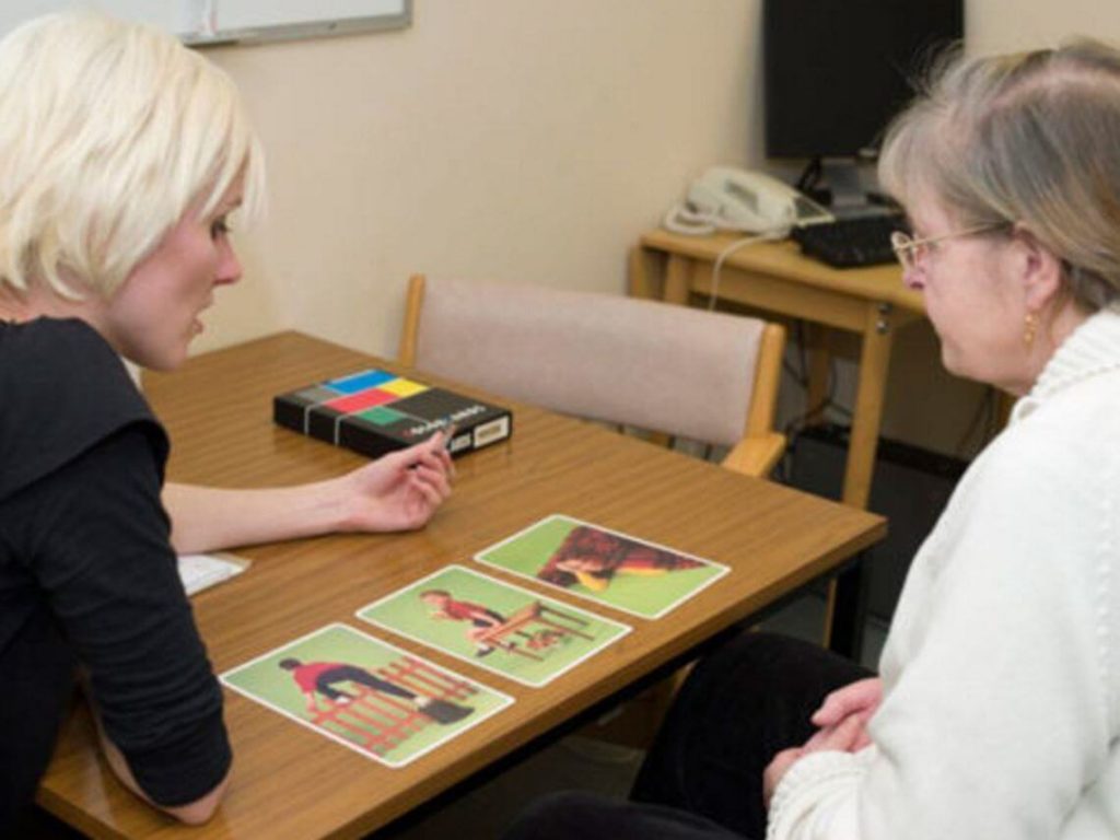 A woman is helping an older patient during speech therapy