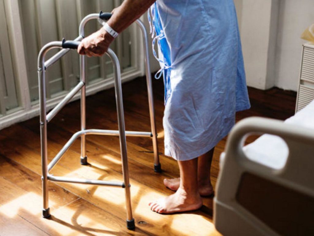 A man walking across the hospital room with his cane