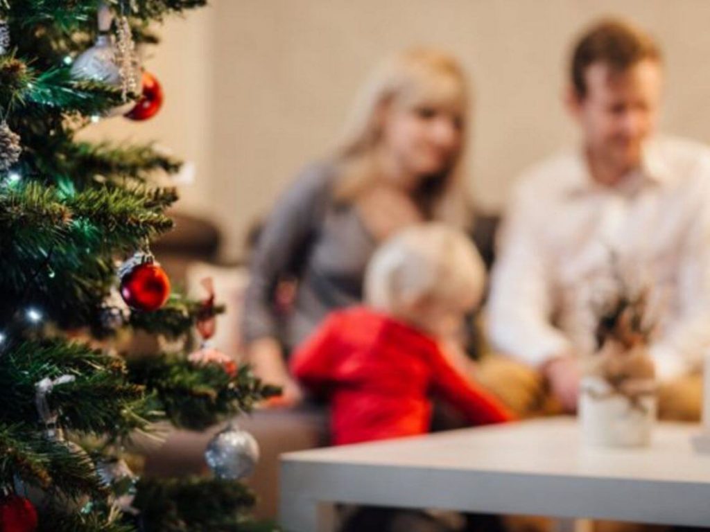 A family sits at a table during christmas time with a tree in the foreground