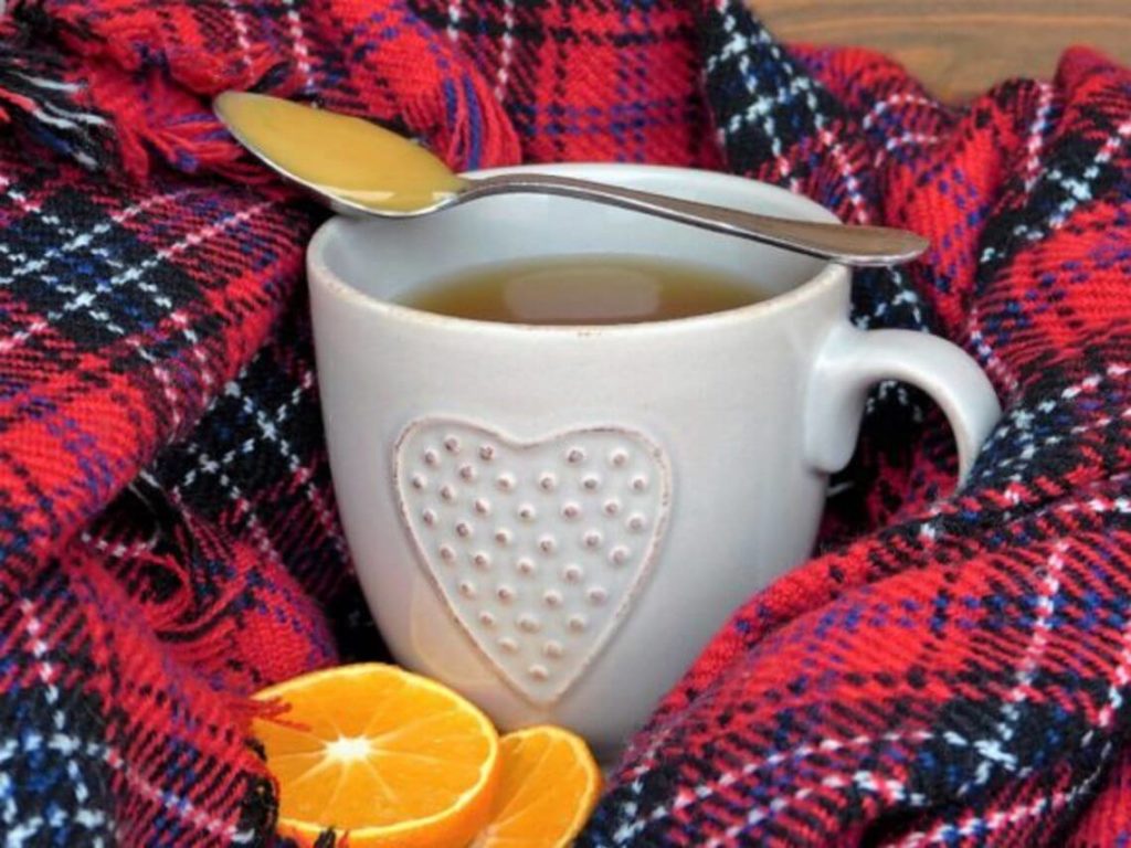 A mug of hot tea with orange slices next to it