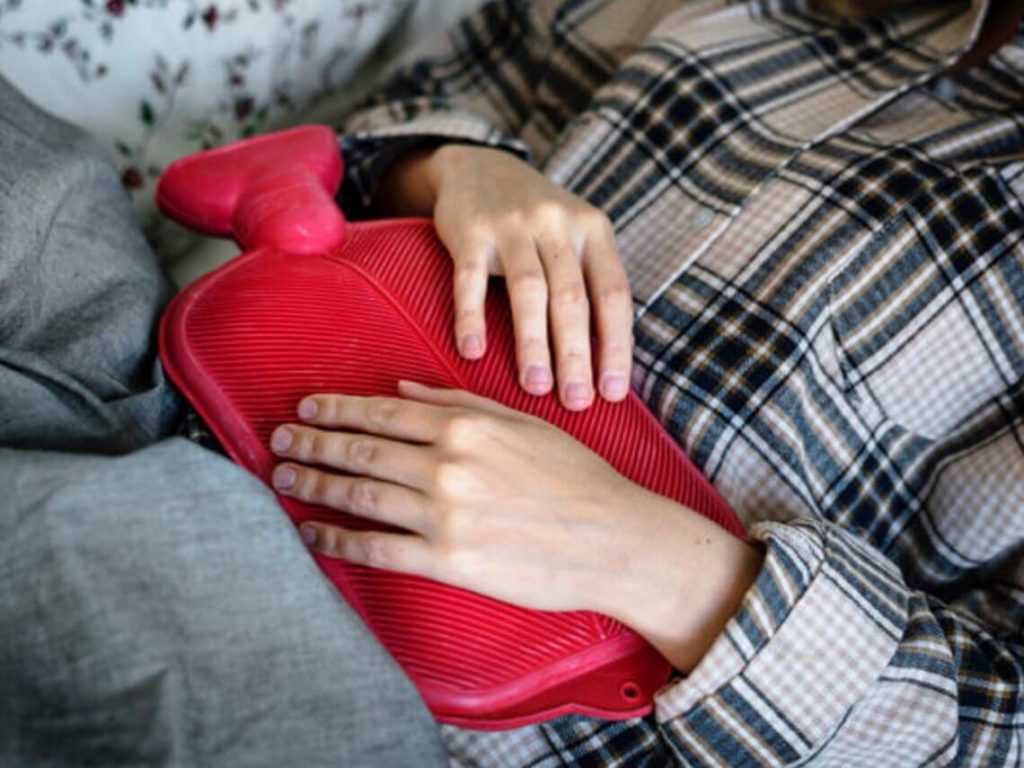 A person lies on a couch while holding a hot compress to stomach