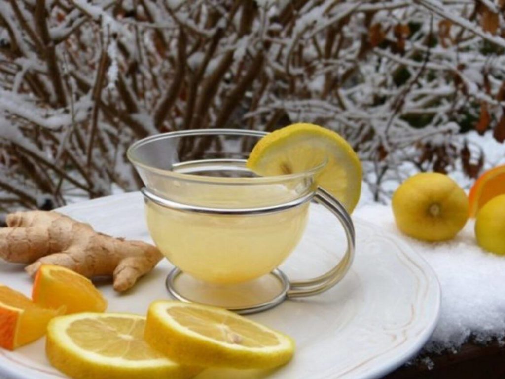 A glass with a lemon wedge on the rip containing a lemon-ginger tea with great care