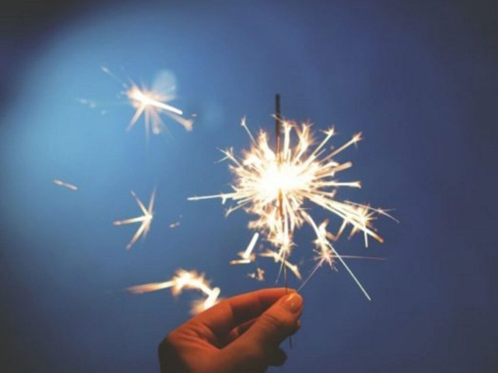 A man is holding a lit sparkler to celebrate the new year