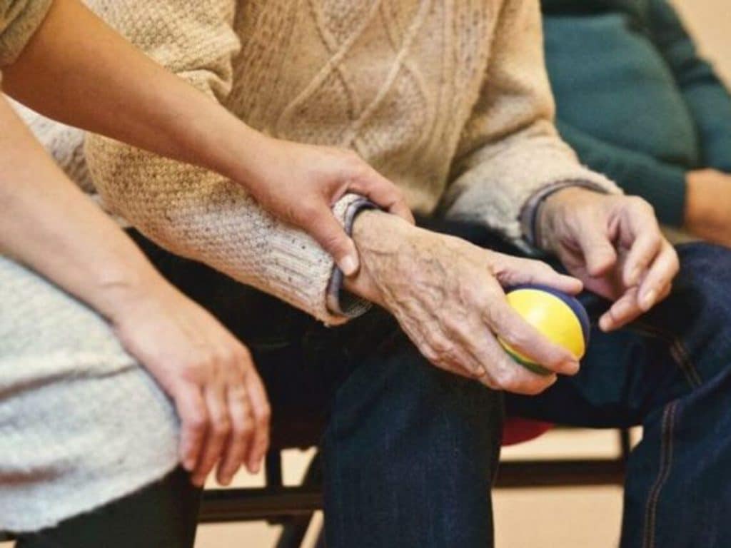 A woman places her hand on a senior male's arm holding a tennis ball after a stroke