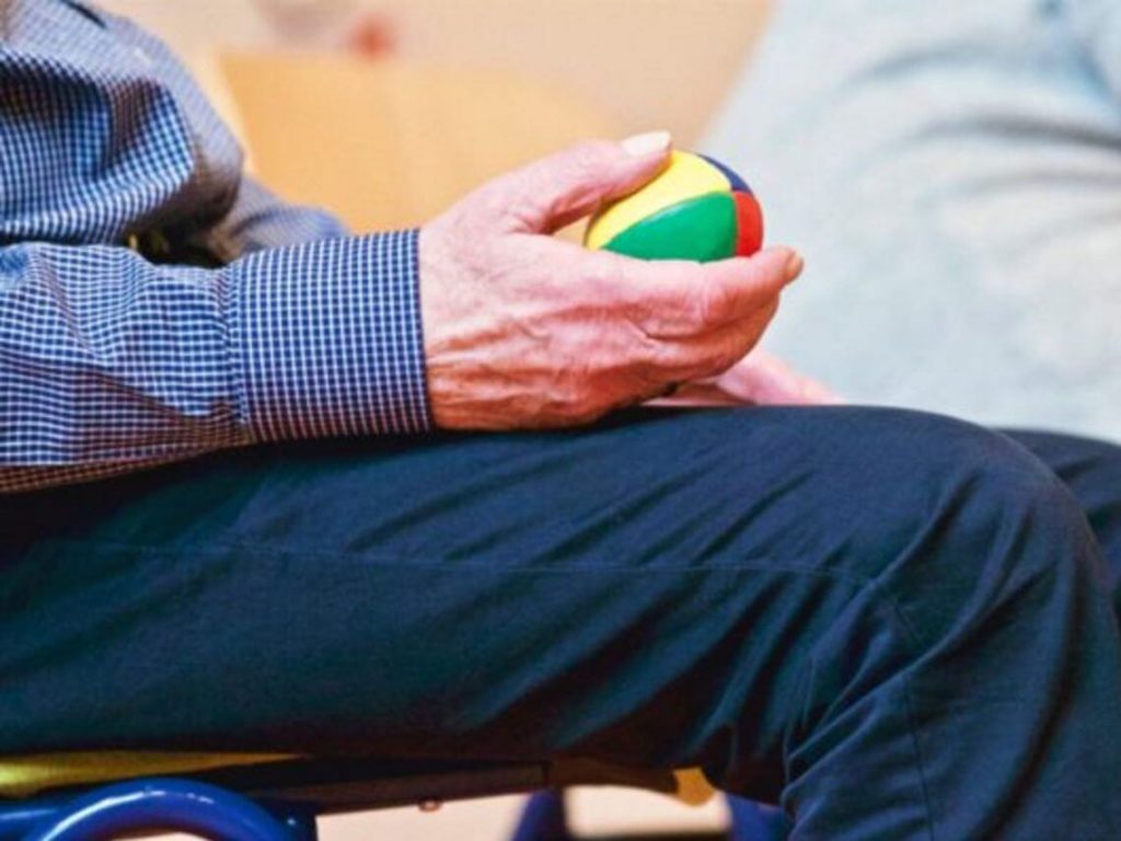 A man holds a colorful ball as he sits in a chair
