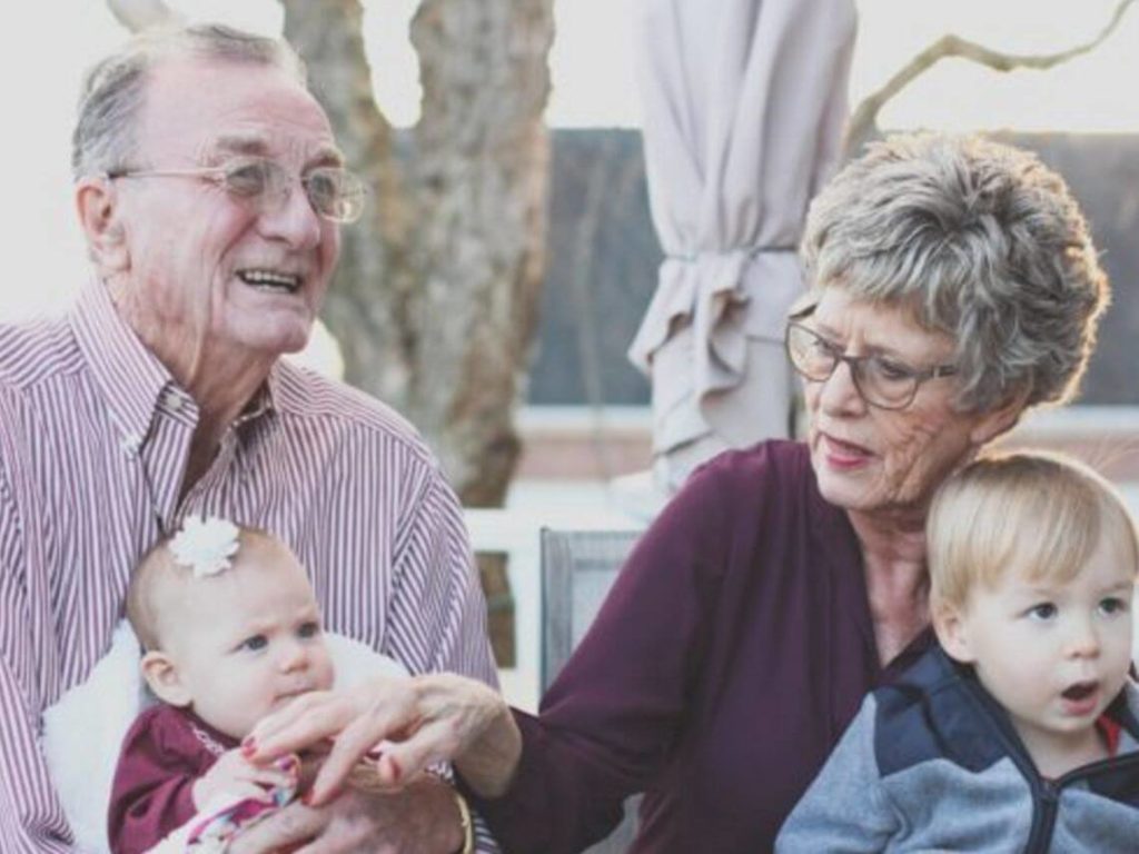 An elderly couple are holding their small grandchildren promoting senior care