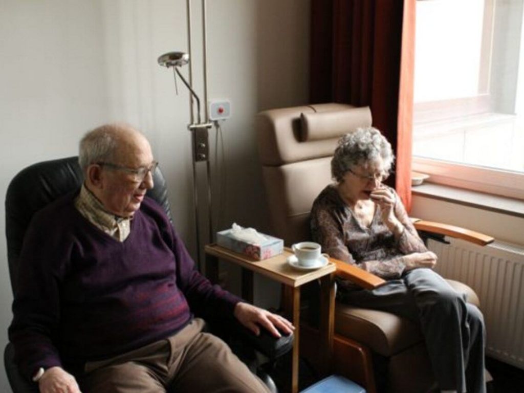 An elderly couple sit next to each other in a nursing home post acute care spending