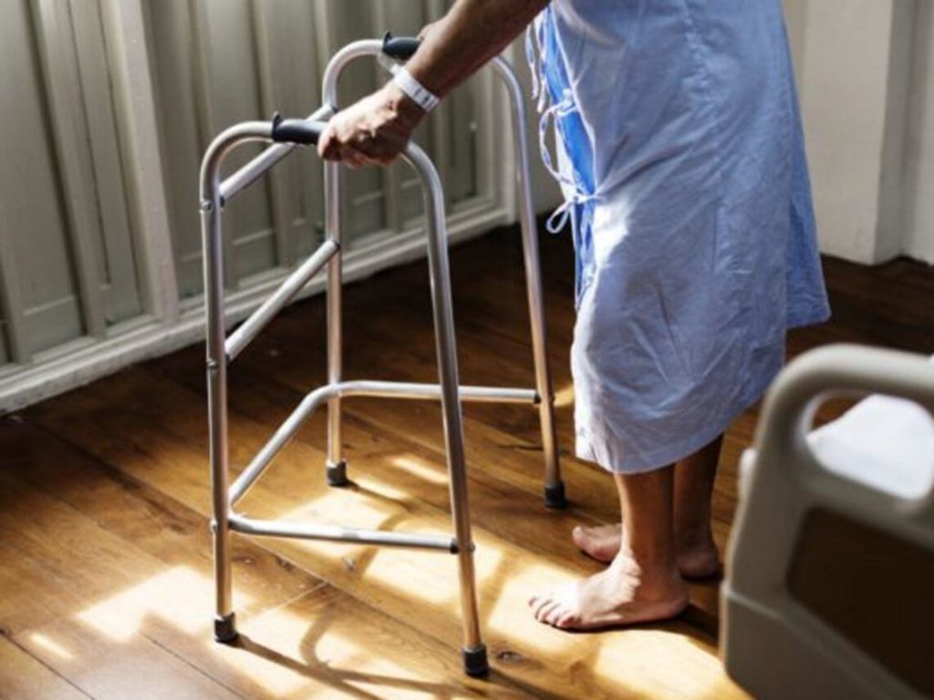 elderly person using walker after injury in hospital gown post-acute care