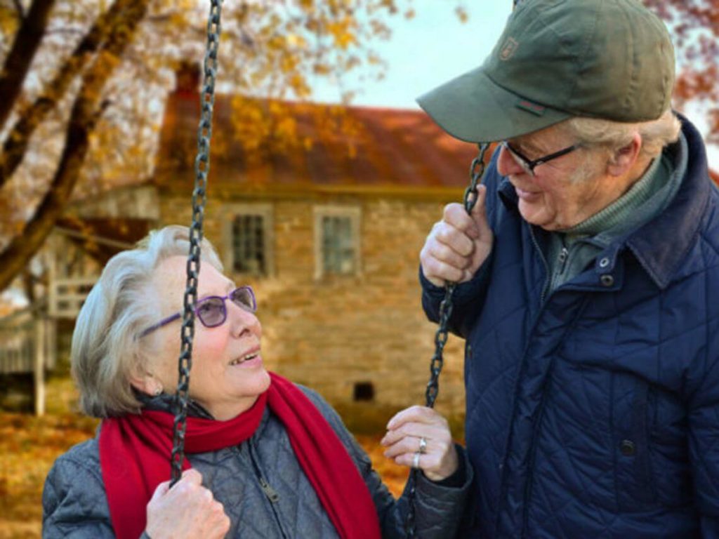 An elderly couple look into each others eyes as the female sits on a swing medicare coverage