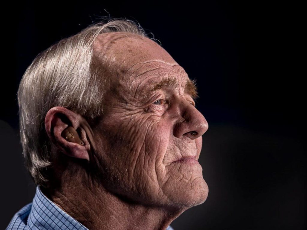 Profile of an Elderly man with hearing aid against a black background