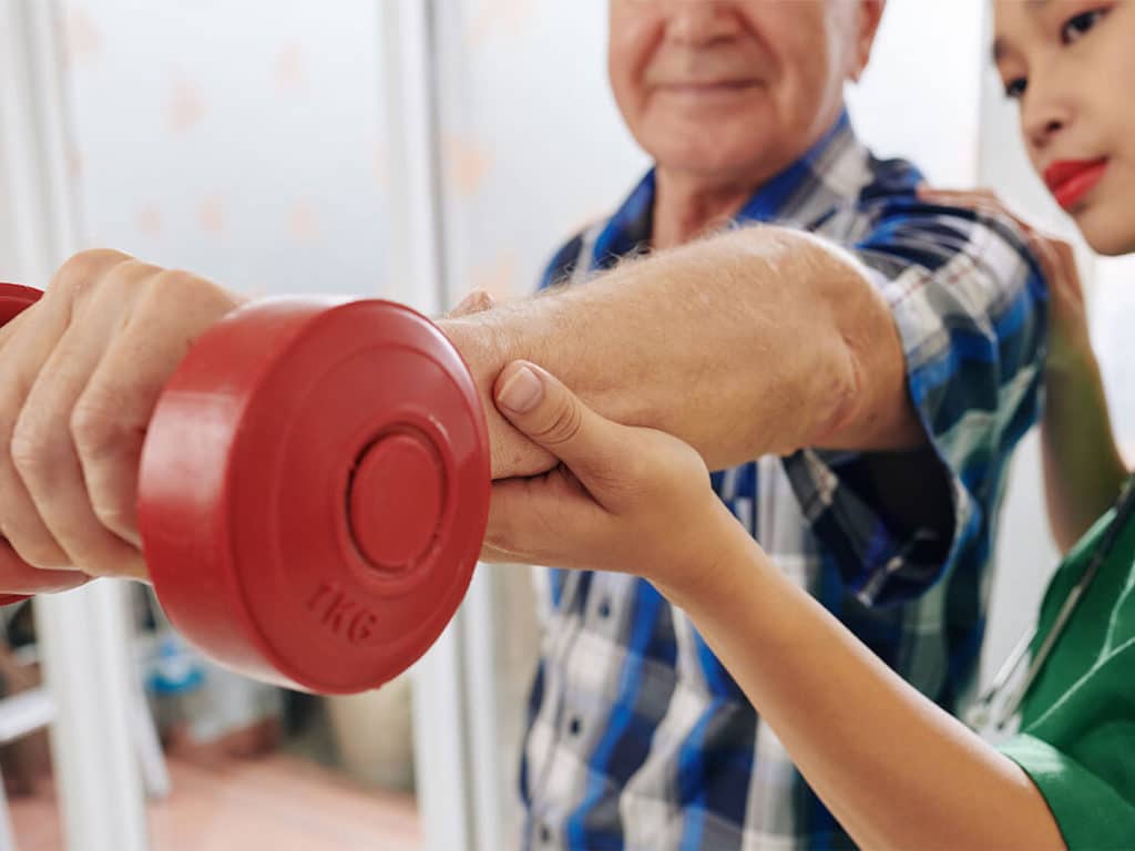 A senior man is lifting weights with the help of a post acute nurse