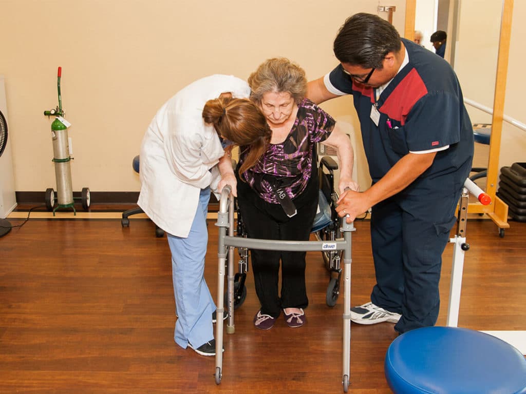 A woman is being helped by two nurses while handling her cane