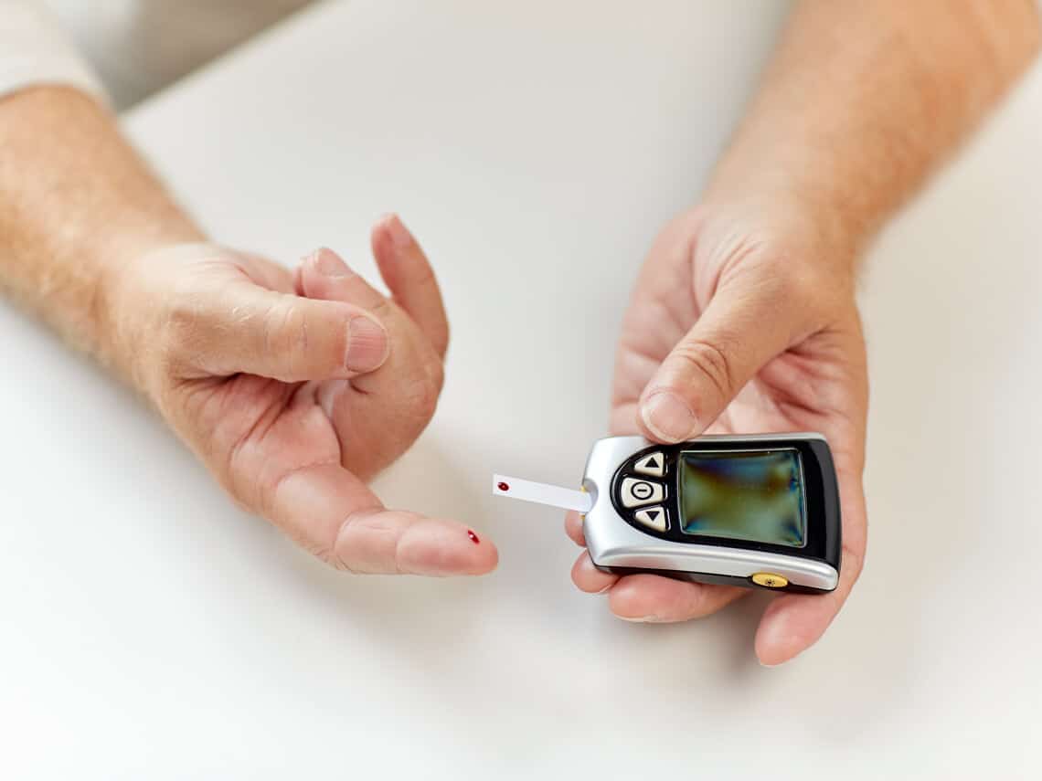 Senior man with diabetes checking blood sugar with glucometer