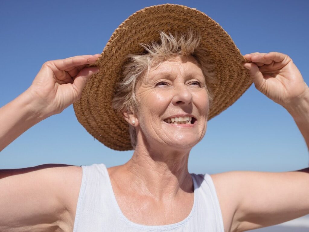 Senior woman smiling in sunlight while holding her hat