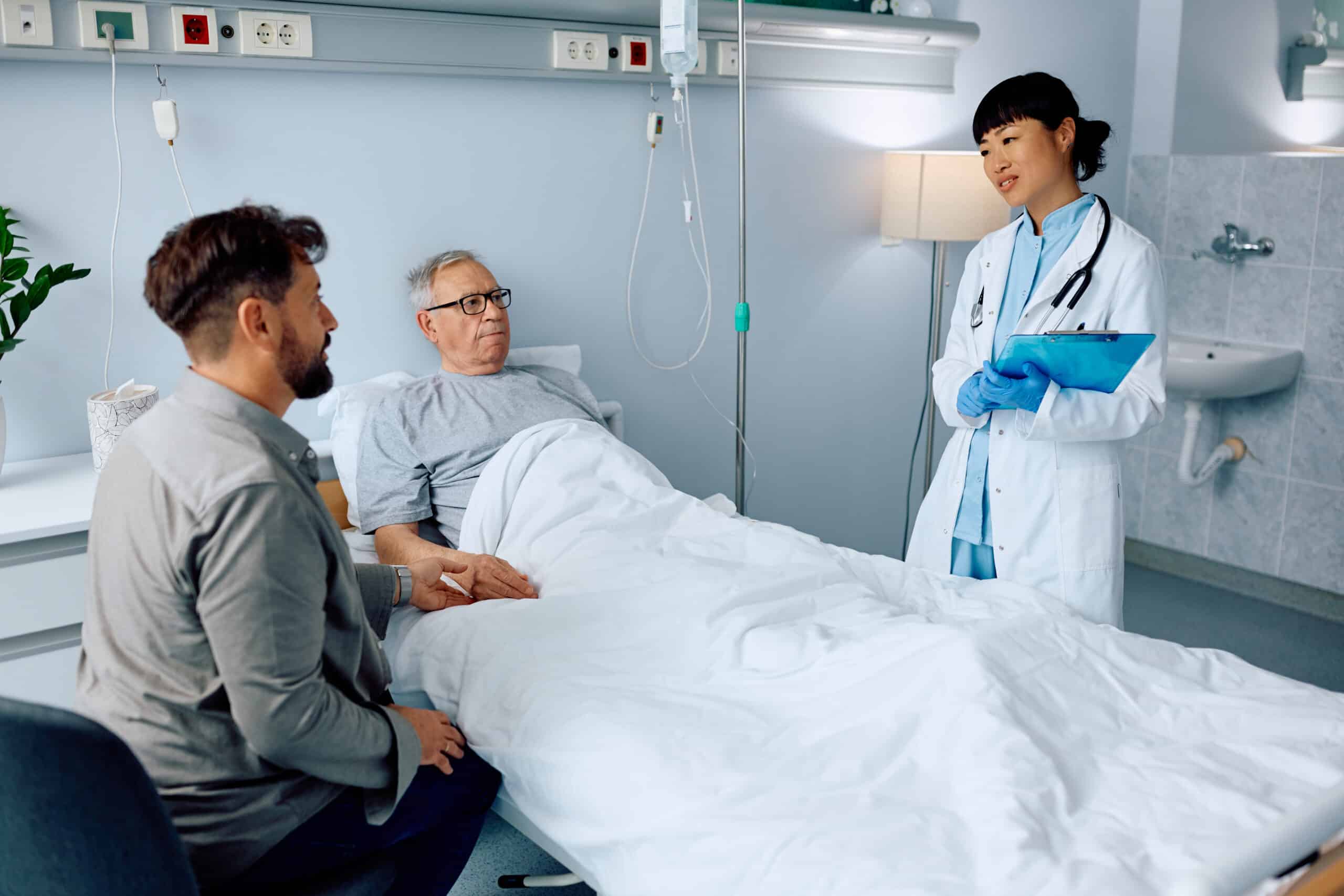Female doctor talking to a senior patient and his son in a hospital room