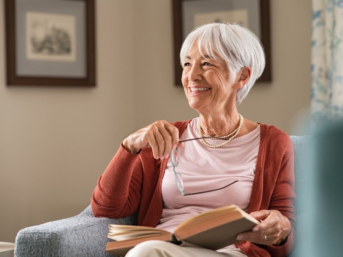 Smiling senior woman holding a book and glasses