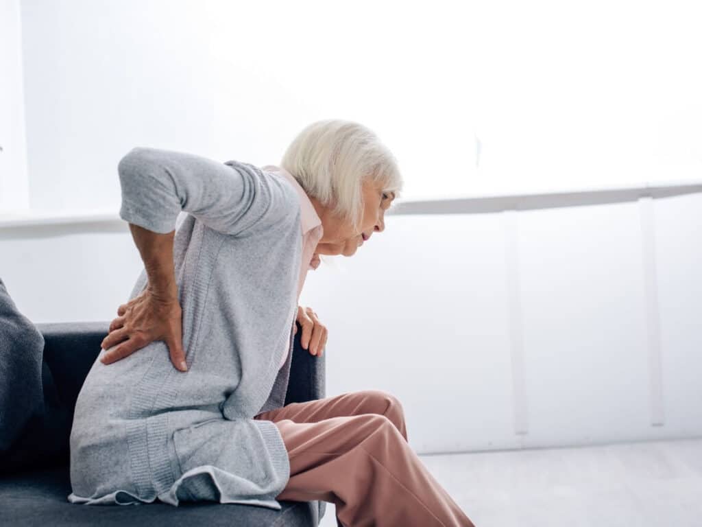 Senior woman with back pain, sitting on couch