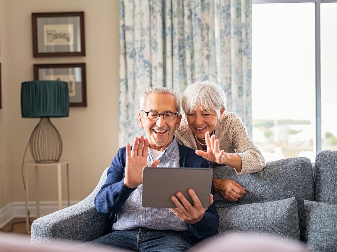 Happy senior couple waving at tablet screen