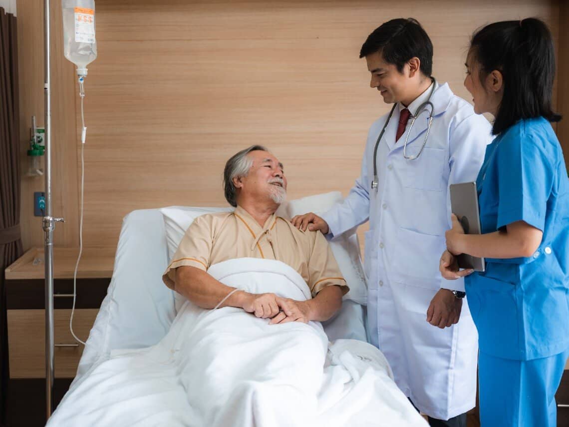 Senior man laying in bed talking to doctor and nurse